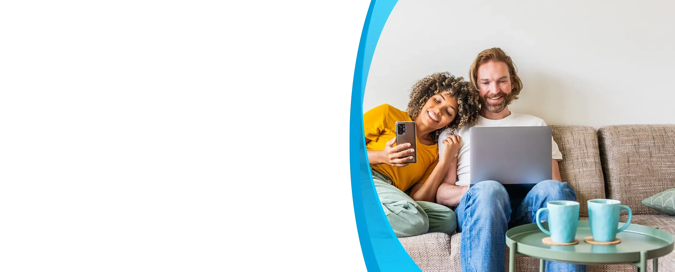 A smiling couple relaxes on a couch sharing a laptop and smartphone together.